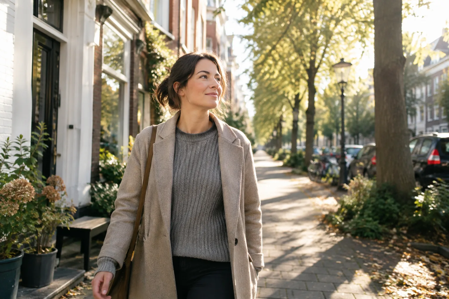 Een vrouw wandelt in de ochtend over een zonnig woonstraatje met bomen; laag warm daglicht valt op haar gezicht.