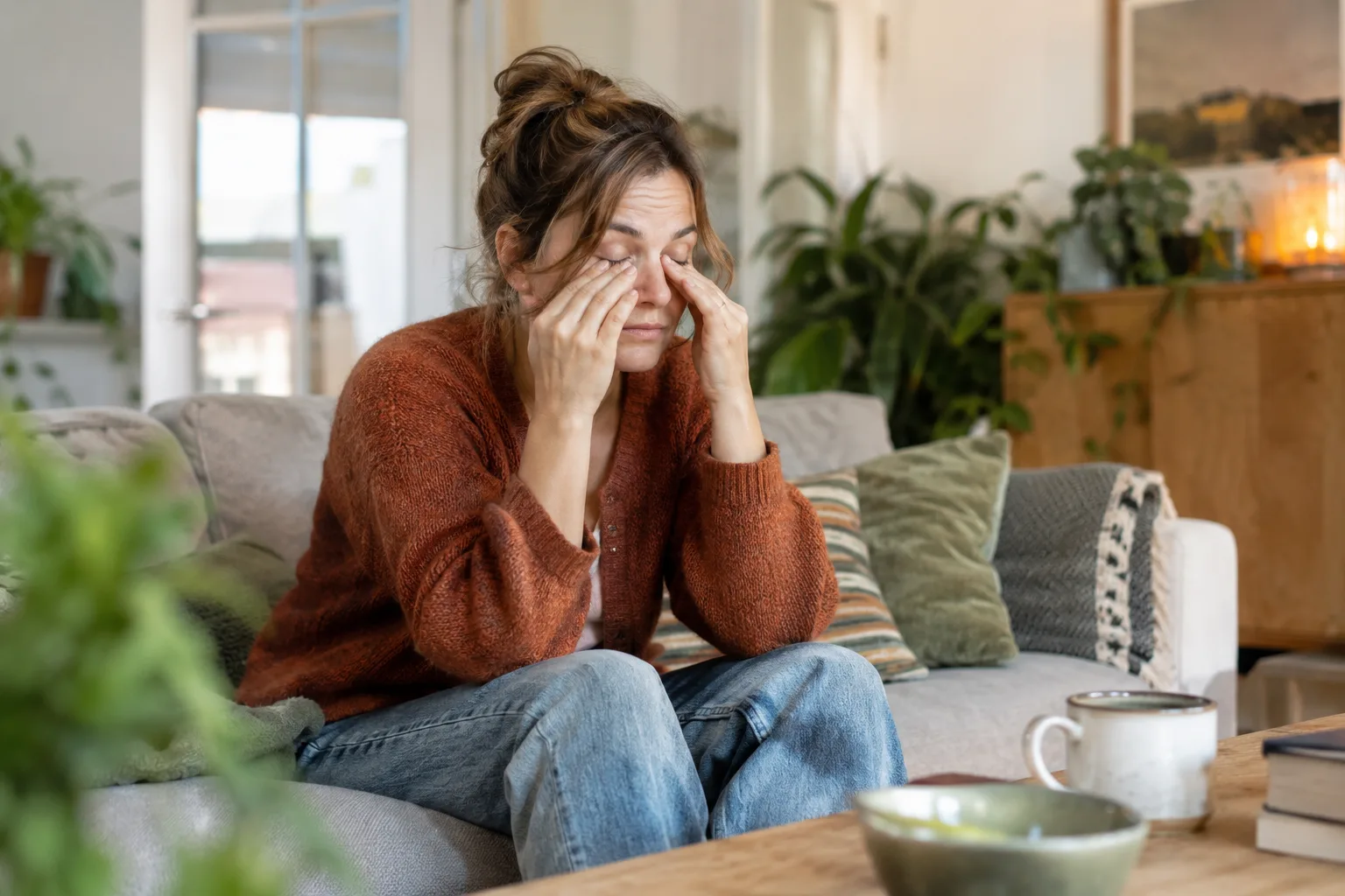 Een volwassen vrouw zit tijdens een rustige middag op een bank en wrijft zacht in haar ogen, geen dramatische uitputting.
